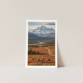 Framed photograph of a mountain landscape with a path and animals in the foreground on a light gray background.
