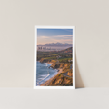Poster of a coastal landscape with mountains on a light gray wall.
