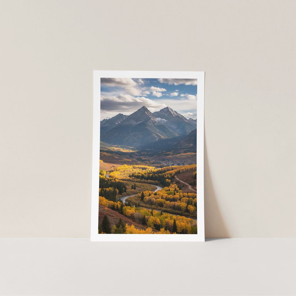 Framed photograph of a mountain landscape with trees and a road on a light gray wall.