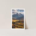Framed photograph of a mountain landscape with trees and a road on a light gray wall.