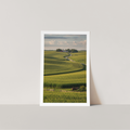 Framed print of a landscape with green fields and a path on a white wall.