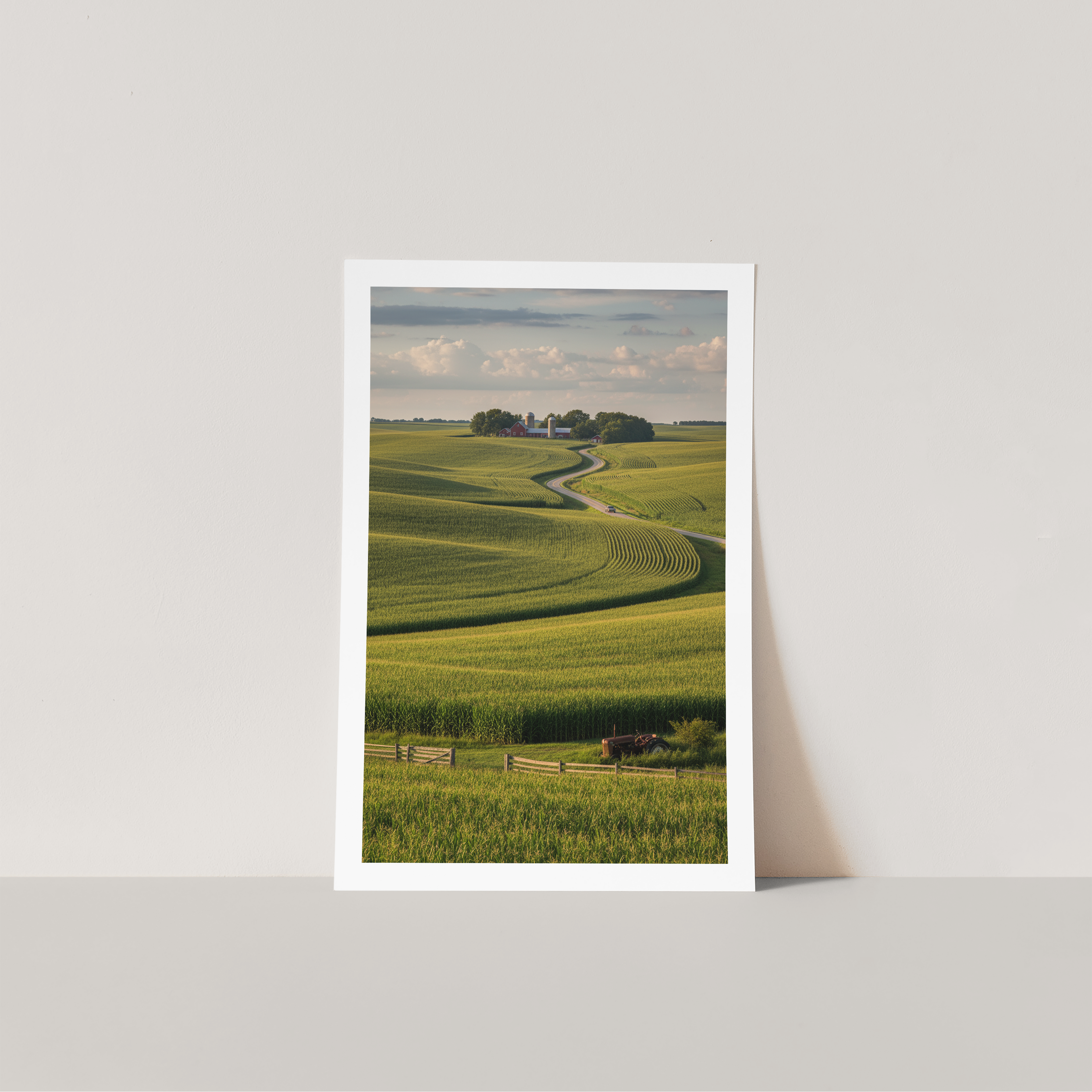 Framed print of a landscape with green fields and a path on a white wall.
