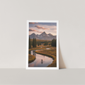 Framed photograph of a mountain landscape with a river and person on a white wall.